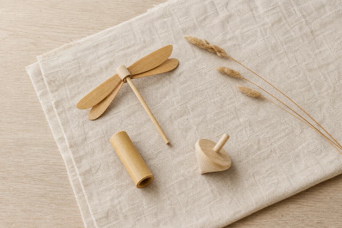 Handmade bamboo dragonfly, bamboo whistle, and wooden spinning top arranged on natural linen with dried grass stems — natural material folk objects from Serein Home Journal