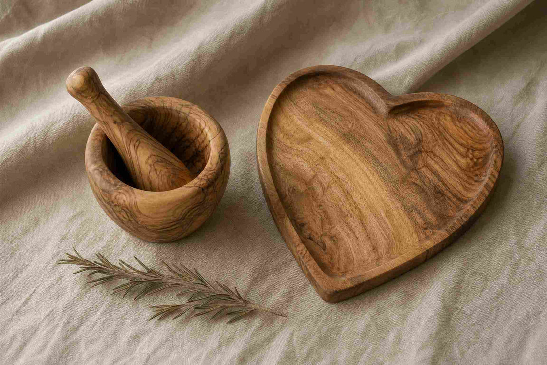 Olive wood mortar and pestle beside an acacia wood heart serving tray on natural linen — a side-by-side comparison of two hardwoods for the kitchen