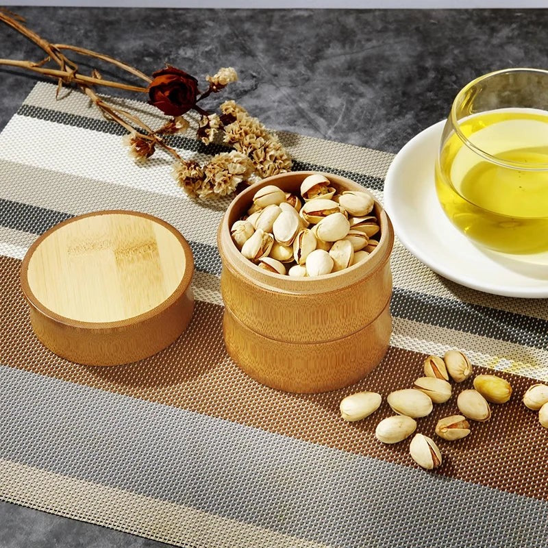 Small bamboo canister holding pistachios next to its round bamboo lid and a cup of tea, Serein Home