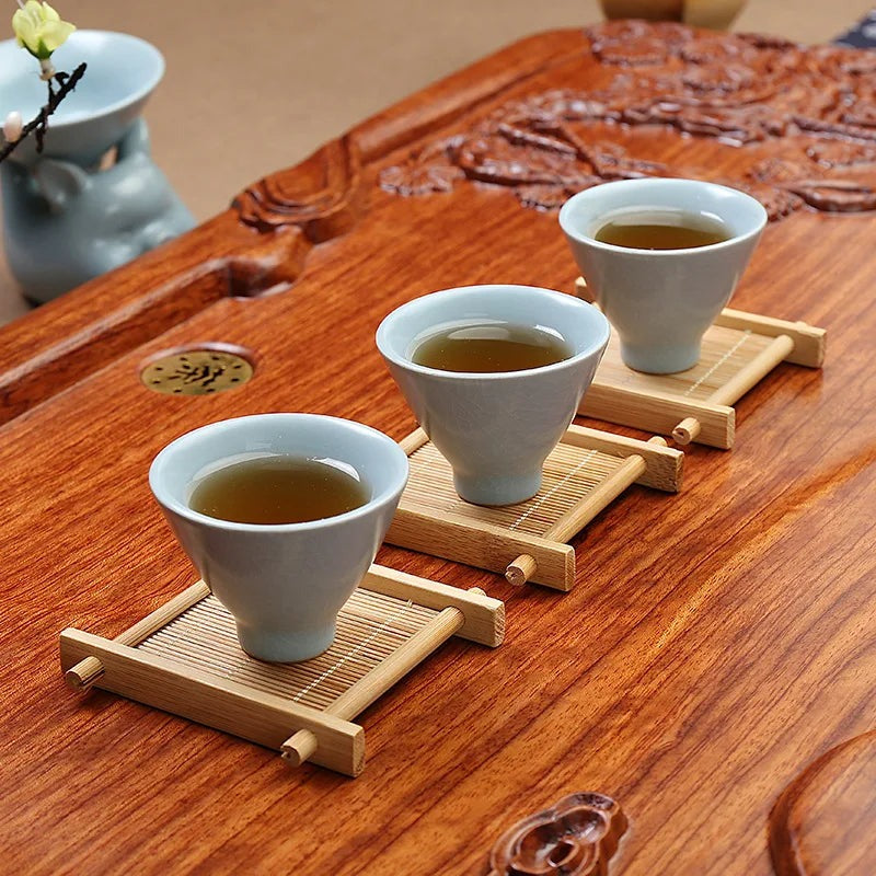 Three celadon tea cups on bamboo cup mats along a carved wooden tea table, Serein Home