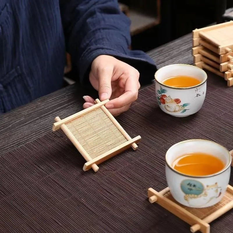 Hand setting a cup of tea down on a square bamboo coaster on a dark table runner, Serein Home