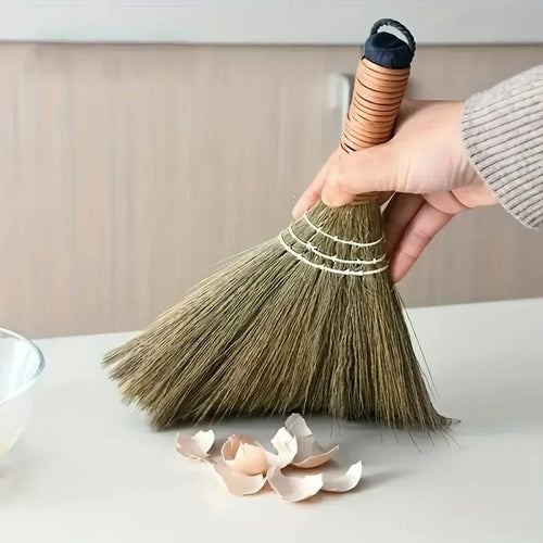 Small grass table broom sweeping eggshells across a white counter