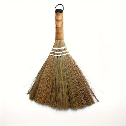Handwoven grass table broom with a bound cane handle on a white background