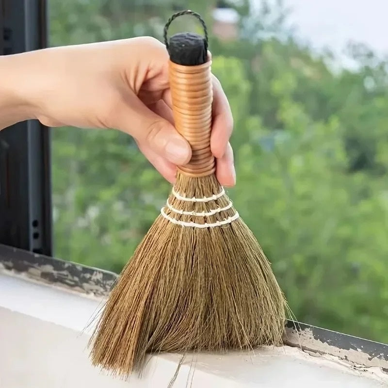 Hand holding a small grass broom against a windowsill