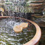 Gourd water dipper floating in a round stone basin below a waterfall