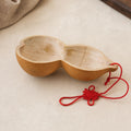 Two-lobed gourd water dipper with a red Chinese knot cord on a pale  plaster surface