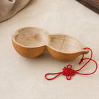 Two-lobed gourd water dipper with a red Chinese knot cord on a pale  plaster surface