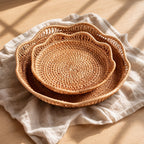 Collection of natural handwoven rattan trays with scalloped edge style on linen surface