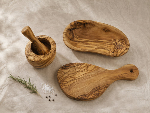 Overhead flat lay of olive wood 3-piece kitchen set with rosemary and peppercorns on linen — mortar and pestle, bowl, and cutting board