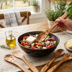 Olive wood kitchen utensils used for tossing salad on a warm kitchen table.