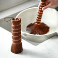 Palm fiber pot brush standing by a white bowl as a second one scrubs inside it, Serein Home