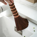 Palm fiber brush sweeping water from a white kitchen sink, showing its fanned bristles, Serein Home