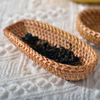 Small oval rattan tray on bedside table with linen and dried botanicals in morning light