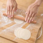 Hands rolling out dumpling wrappers with a slim wooden rolling pin