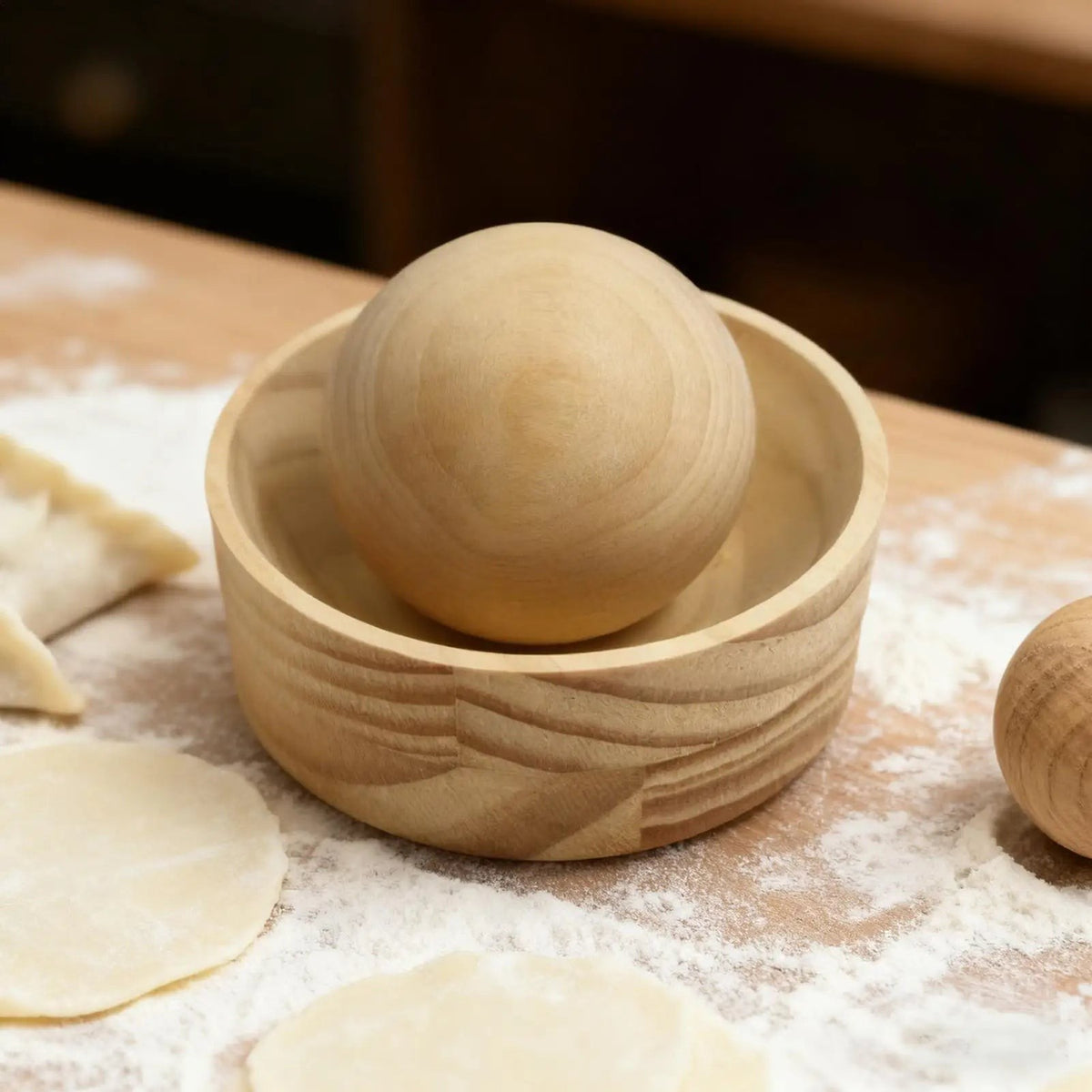 Wooden dumpling wrapper press, a shallow cup holding a wooden ball, on a floured board with dough, Serein Home