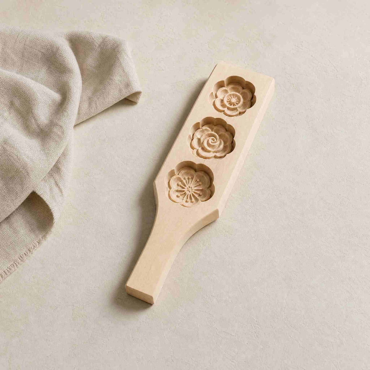 Wooden mooncake press mold with three carved flower patterns on a pale  plaster surface