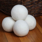 Four extra large New Zealand wool dryer balls stacked on a wooden floor beside a wicker laundry basket - Serein Home