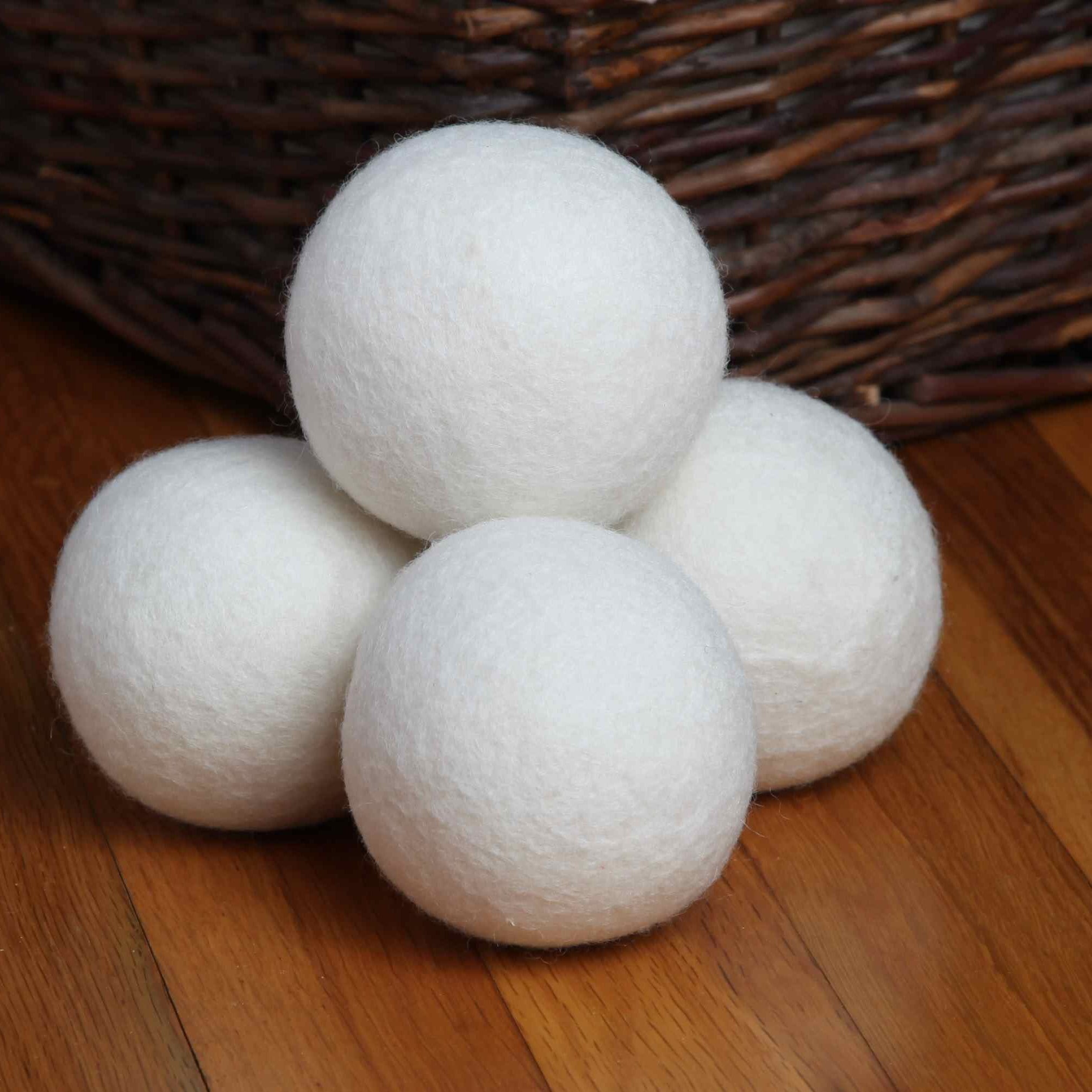 Four extra large New Zealand wool dryer balls stacked on a wooden floor beside a wicker laundry basket - Serein Home