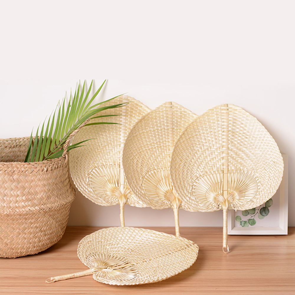 Four woven palm leaf fans beside a seagrass basket and a palm frond