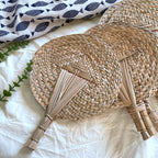 Two woven palm leaf fans with bound stick handles on white linen