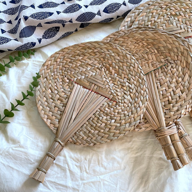 Two woven palm leaf fans with bound stick handles on white linen